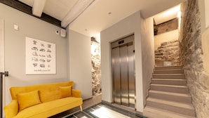 A modern interior with a yellow sofa, an elevator, and a staircase with stone walls. - Hotel Mura 5&7 (Trieste)