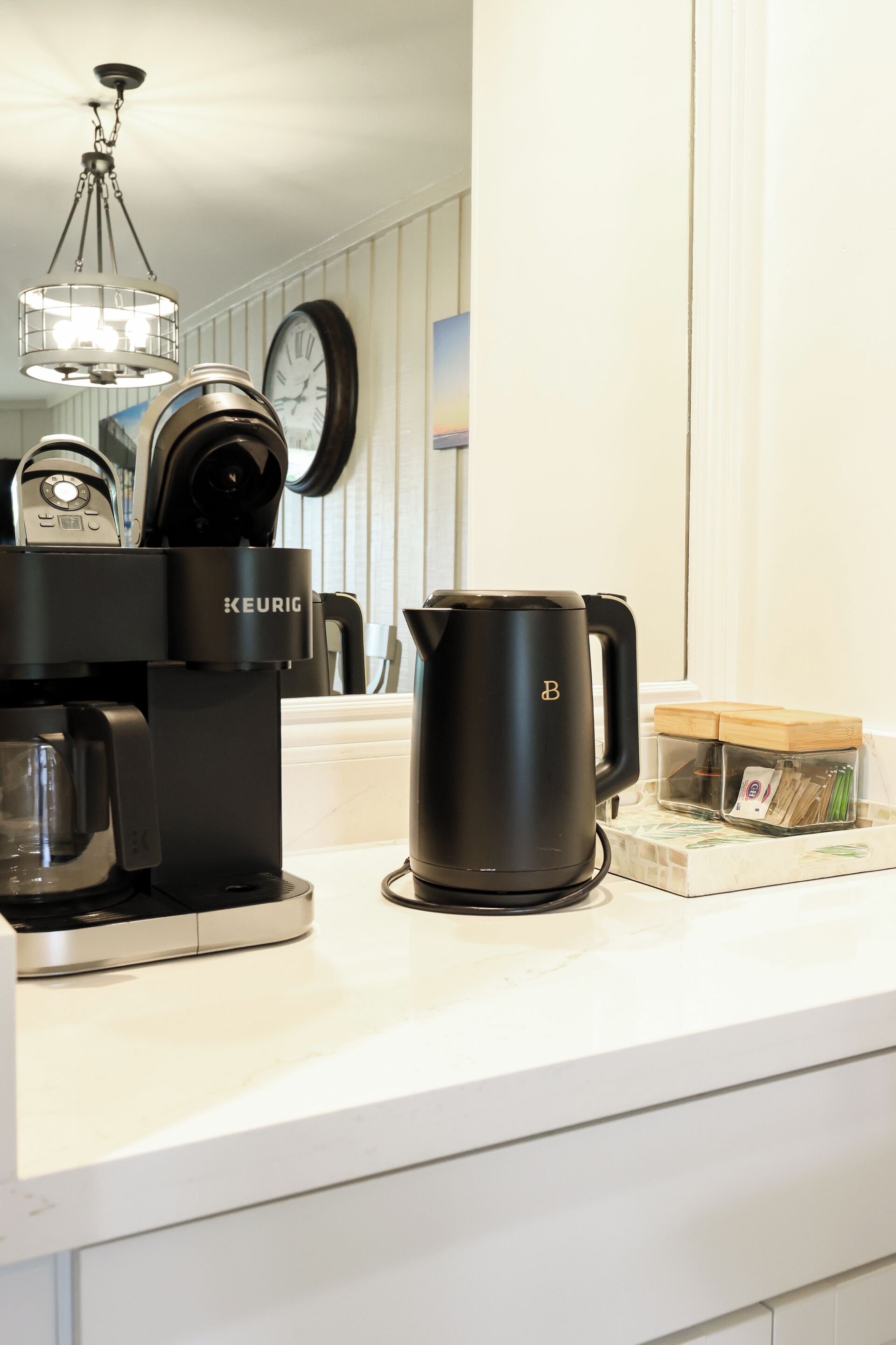 A kitchen counter with a Keurig coffee maker, a black coffee pot, and a coffee maker on a white countertop.