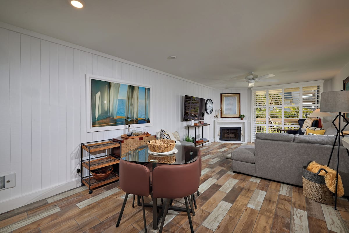 A living room with a sofa, a dining table with chairs, a fireplace, and a large painting on the wall.