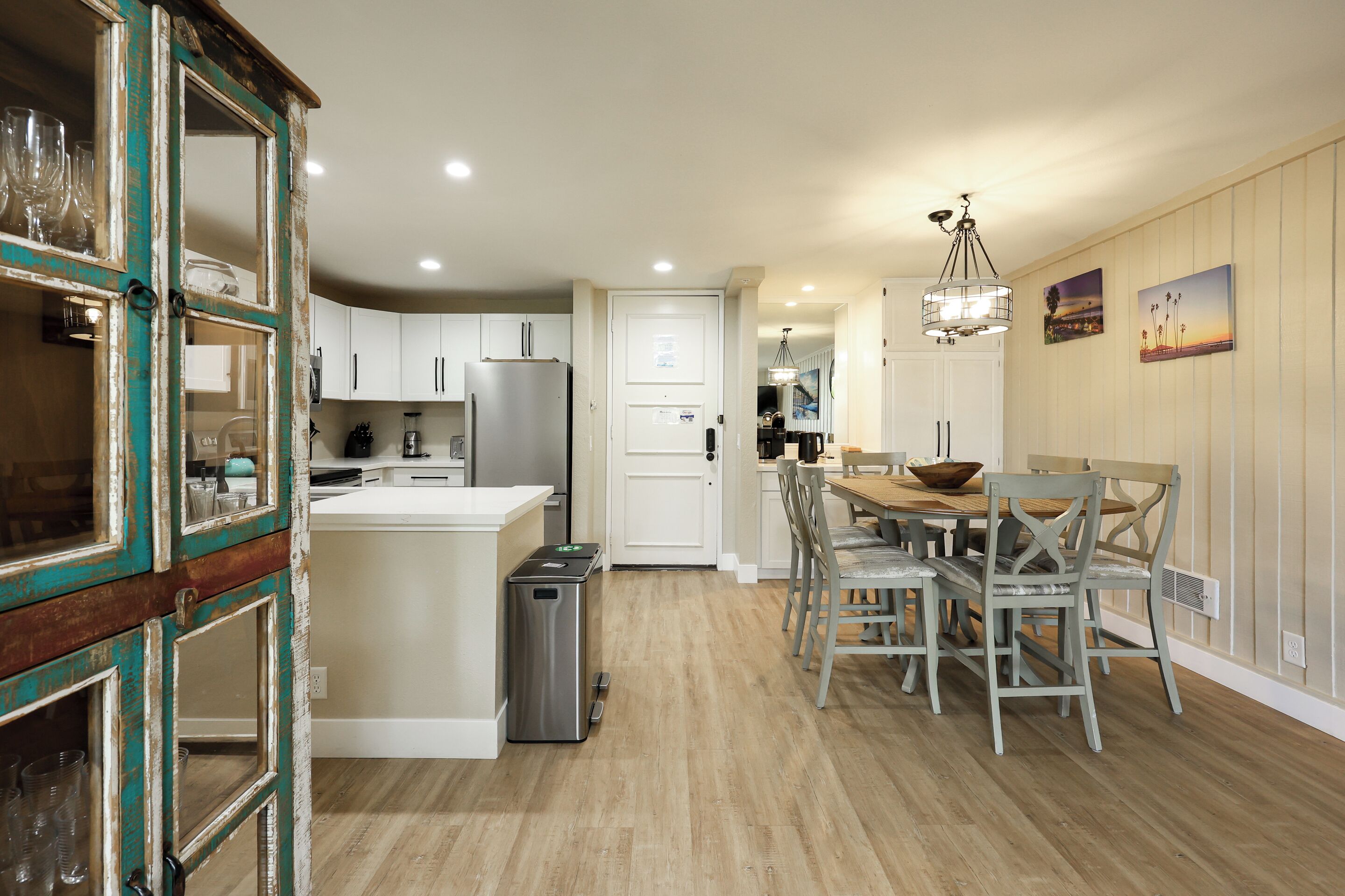 A kitchen with white cabinets, a stainless steel refrigerator, and a dining area with a wooden table and chairs.