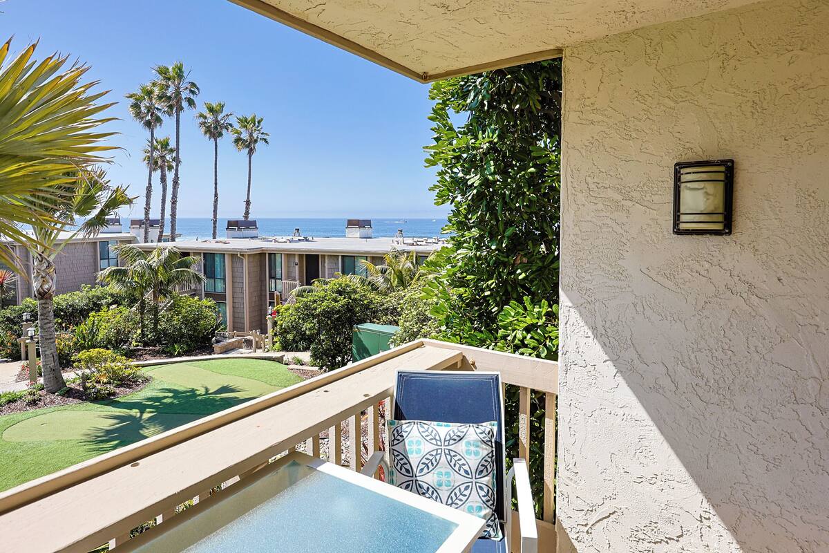 A balcony with a pool, palm trees, and a view of the ocean.
