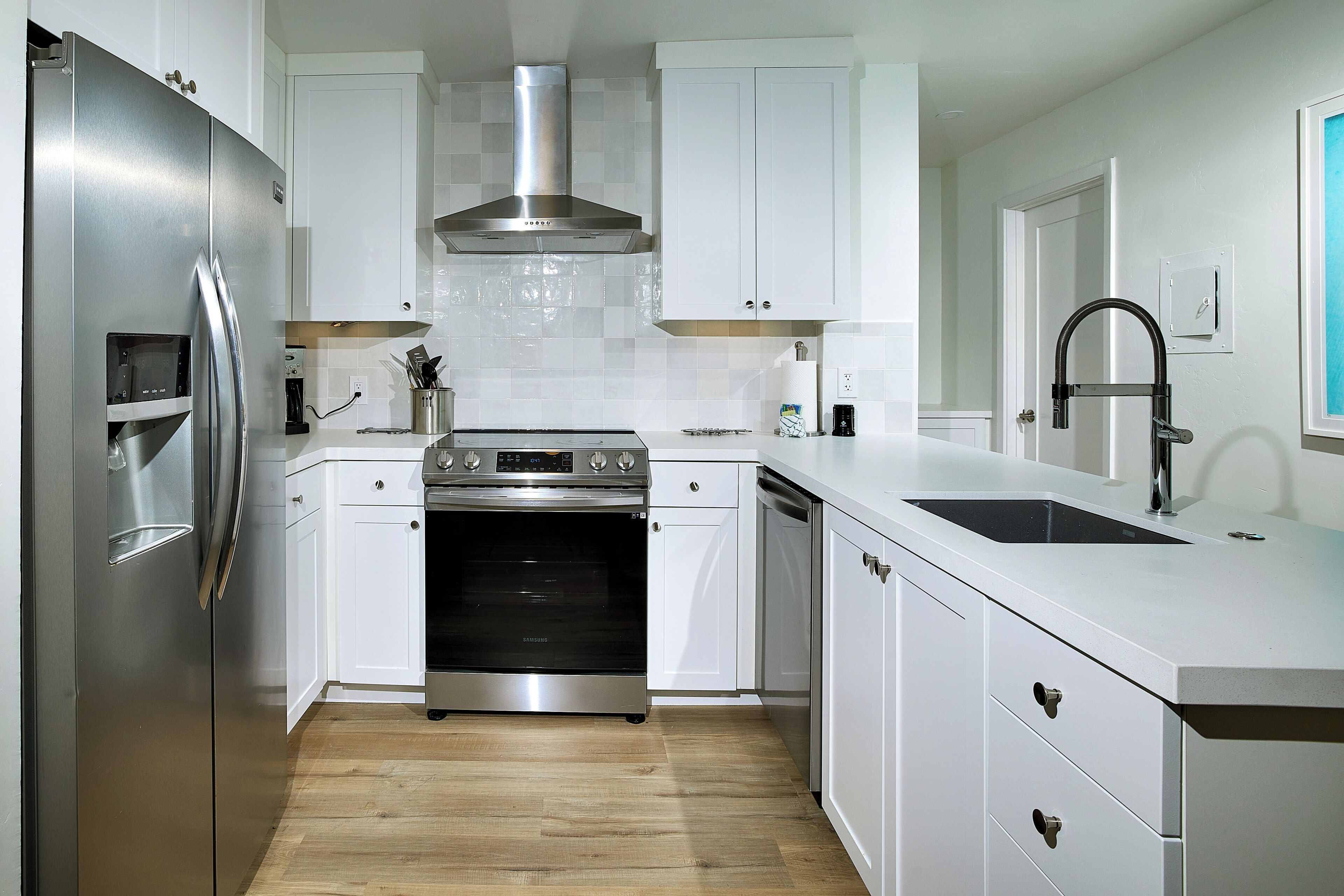 A modern kitchen with white cabinetry, stainless steel appliances, and a wooden floor.