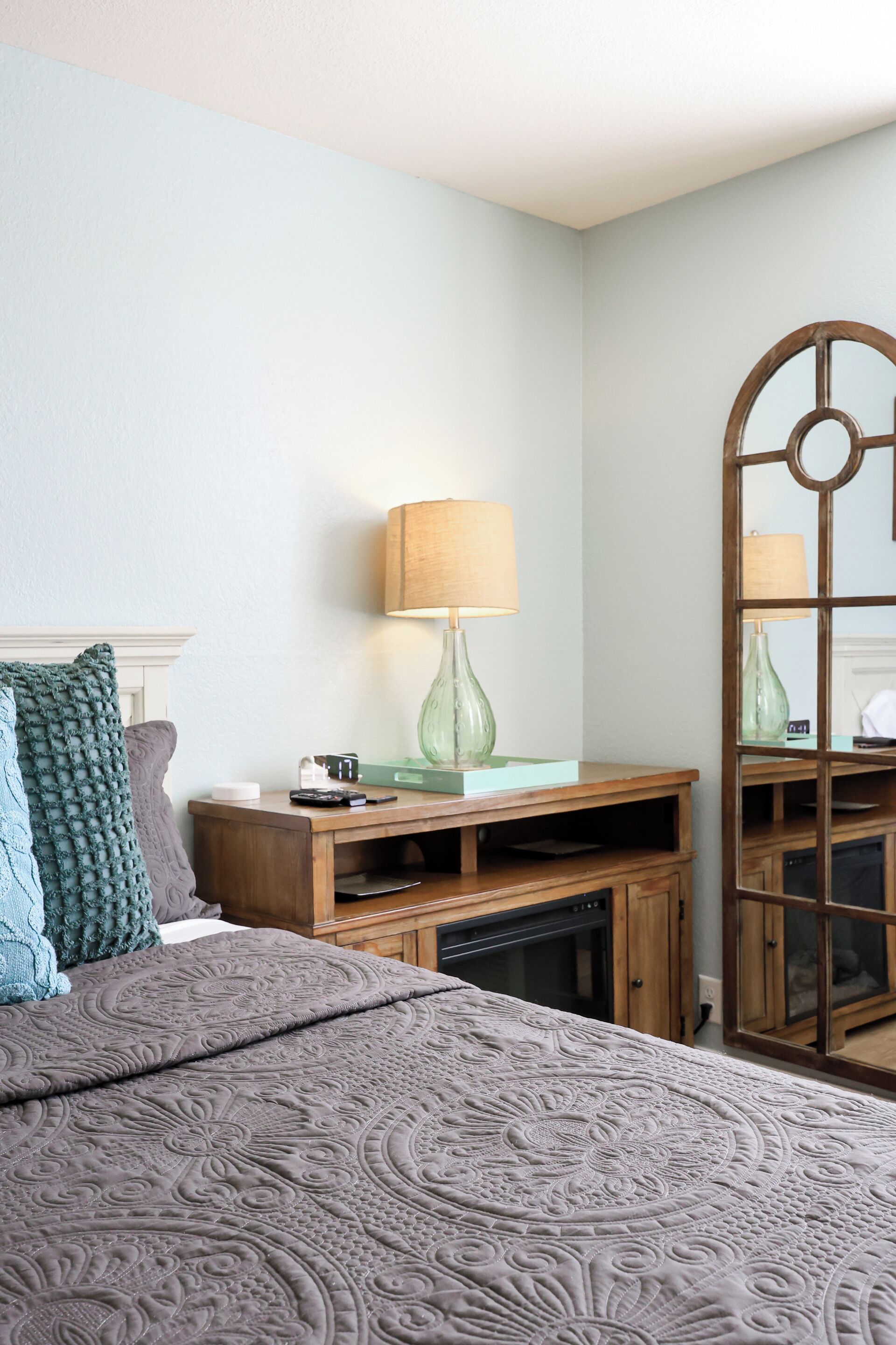 Un dormitorio con cama, una mesita de noche de madera, una lámpara y un espejo.