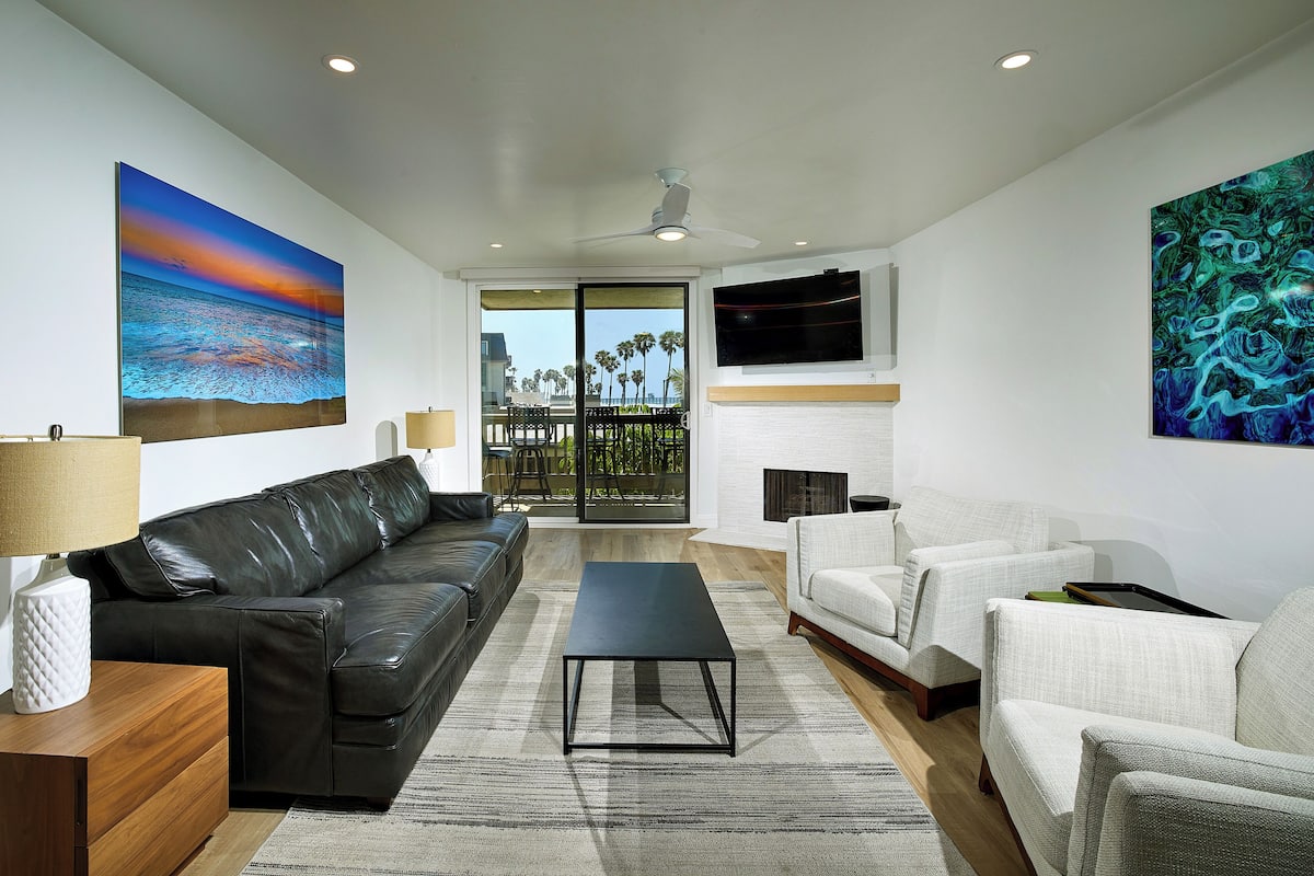 A modern living room with a black leather sofa, a white armchair, a black coffee table, and a fireplace.