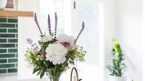 A kitchen counter with a vase of flowers, a metal pitcher, and a wooden tray.