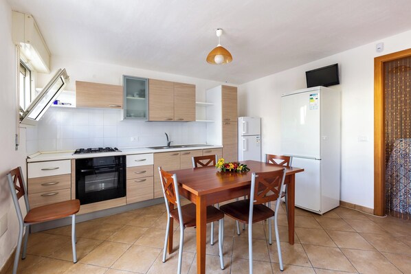 Una cocina compacta con mesa de comedor, sillas, refrigerador y horno empotrado.