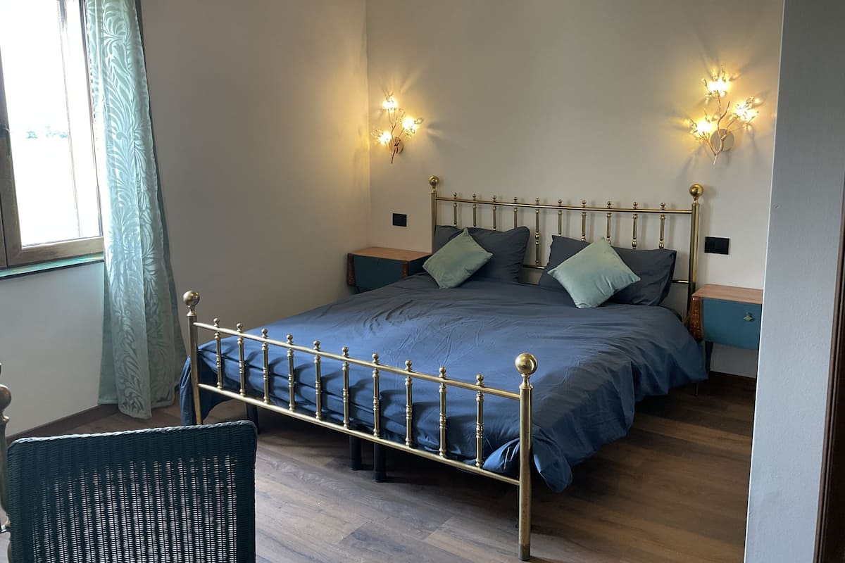 A bedroom with a bed, nightstands, a chair, and wall-mounted lights.