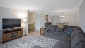 A living room with a TV, sofa, rug, and a dining area with chairs and a table. - Renae Hunt Property (Merritt Island)