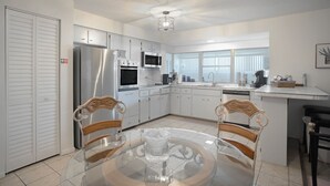 A modern kitchen with white cabinets, stainless steel appliances, and a glass dining table. - Renae Hunt Property (Merritt Island)
