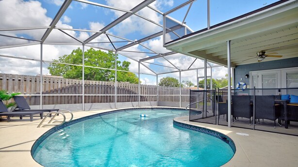 A covered outdoor swimming pool with a glass ceiling, lounge chairs, and a bar area. - Renae Hunt Property (Merritt Island)