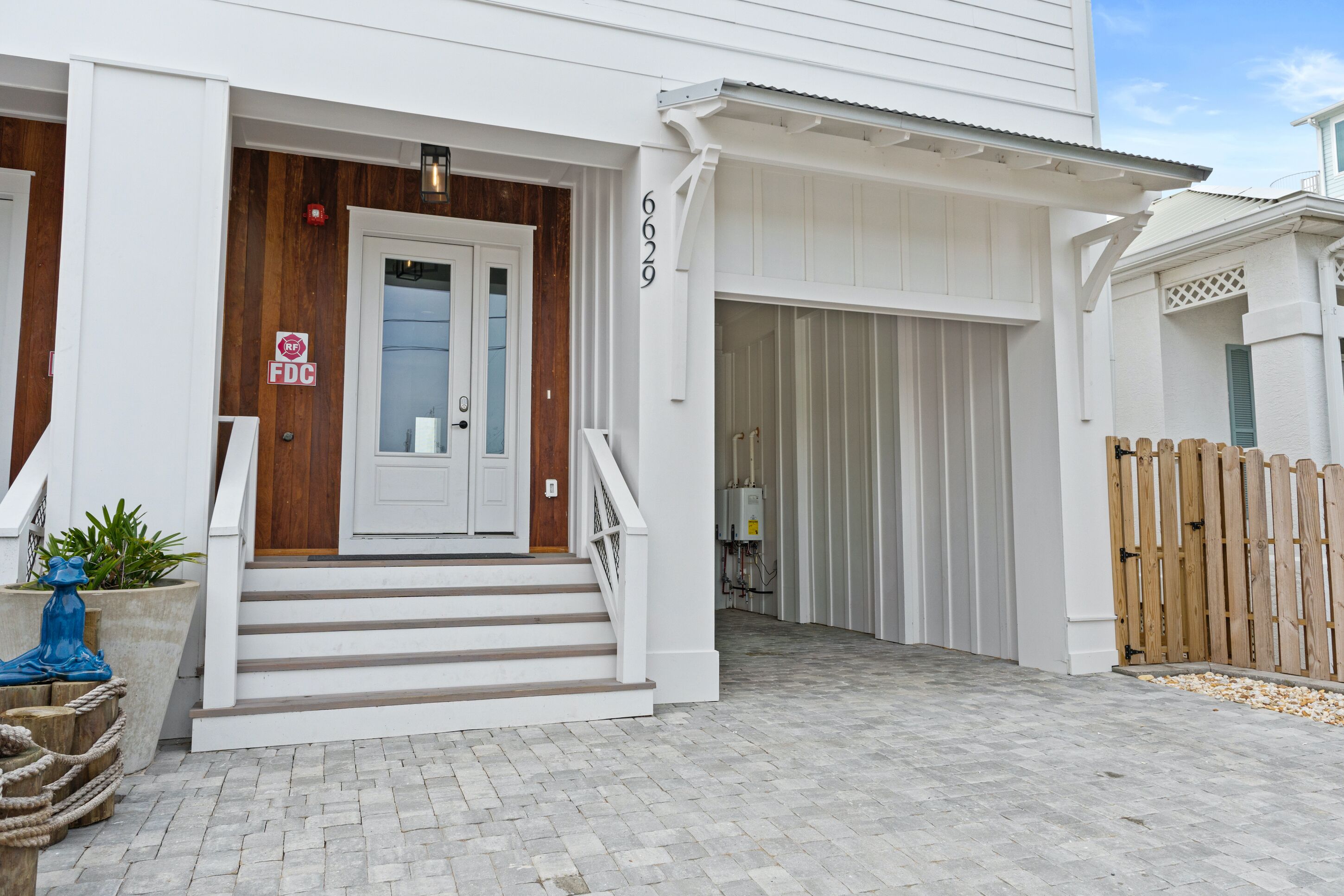 A white building with a wooden front door, a staircase leading to the entrance, and a garage door.