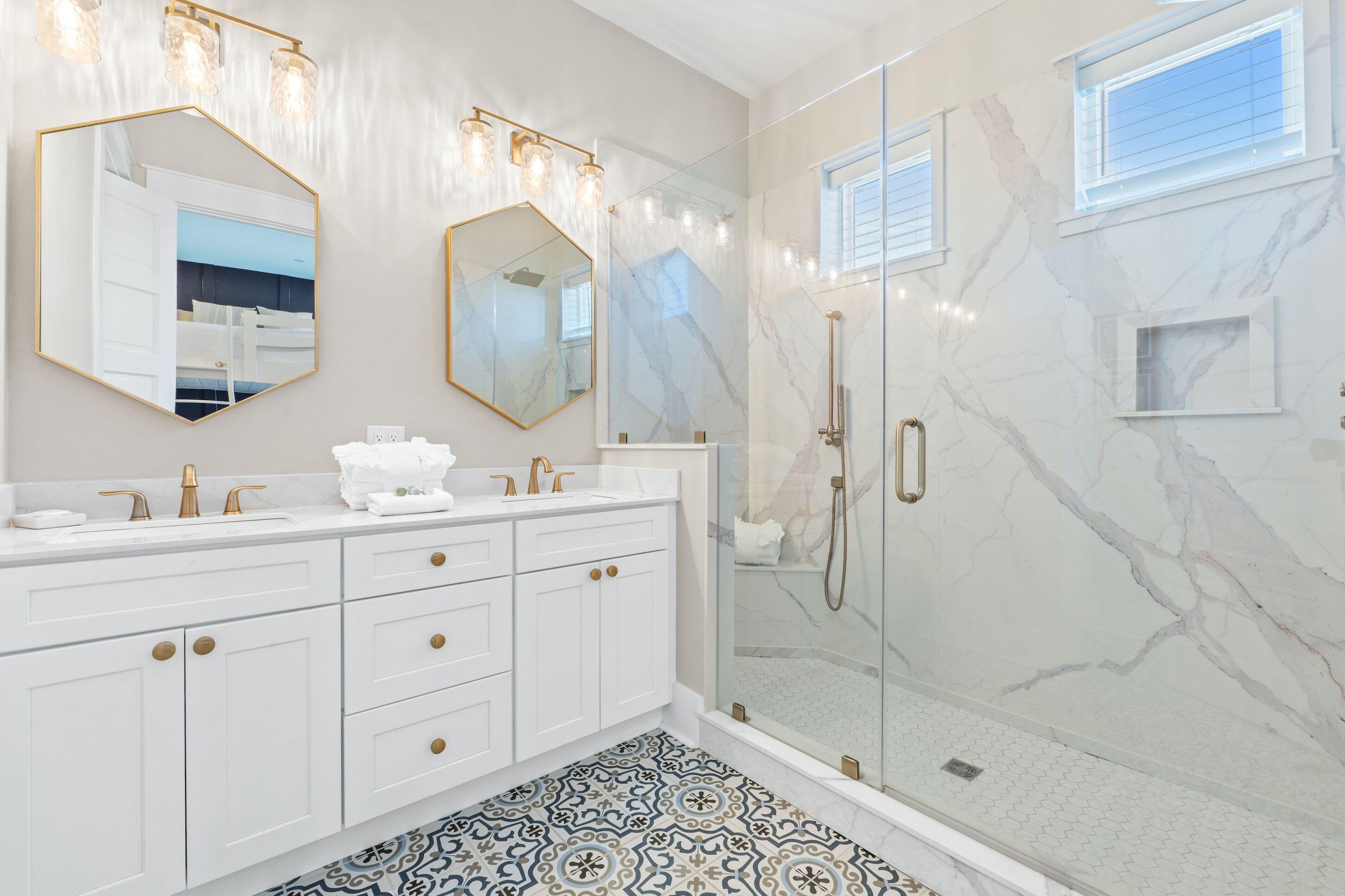 A modern bathroom with a glass-enclosed shower, white cabinetry, and a patterned floor.