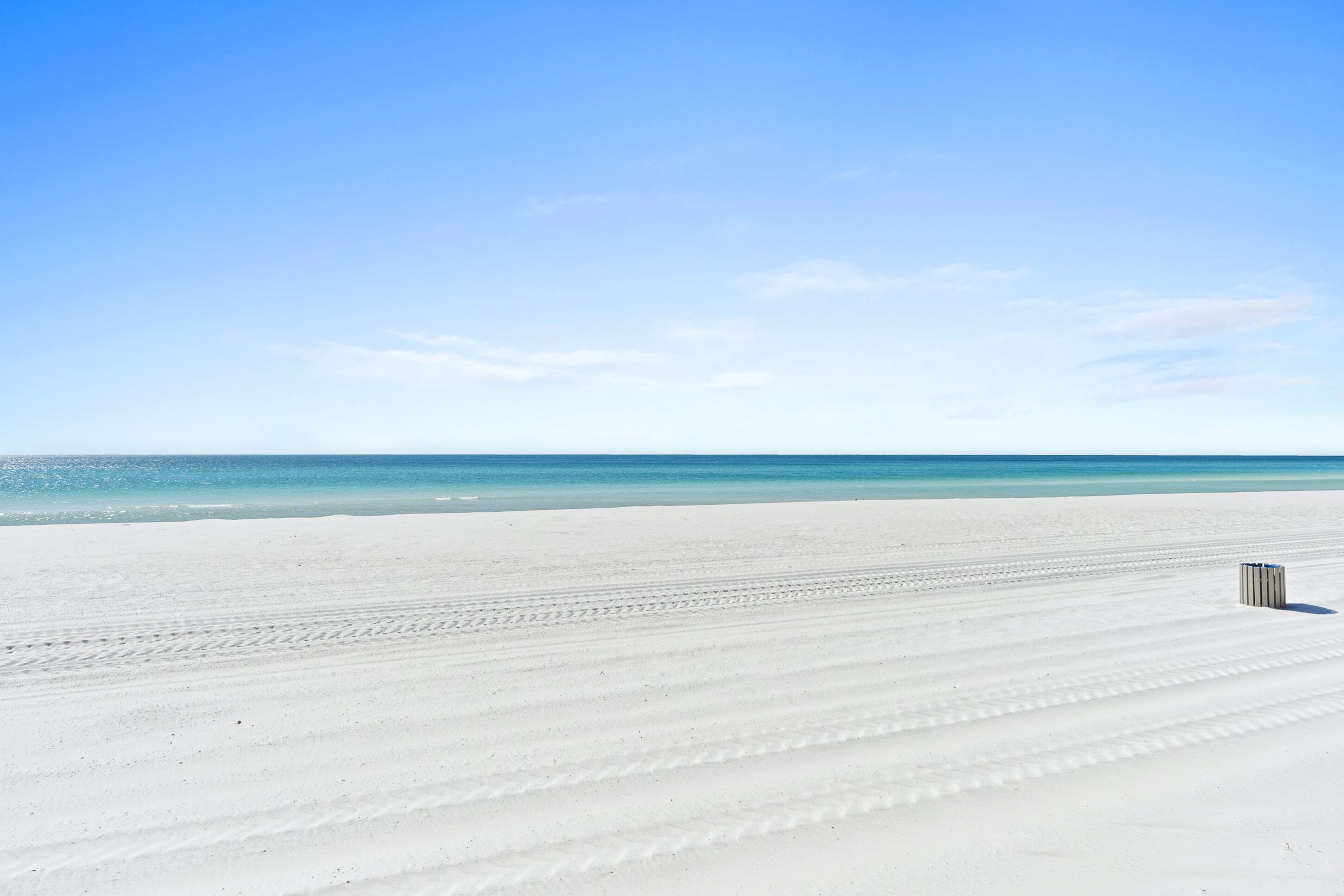 A wide, white sandy beach with a clear blue sky and calm ocean.
