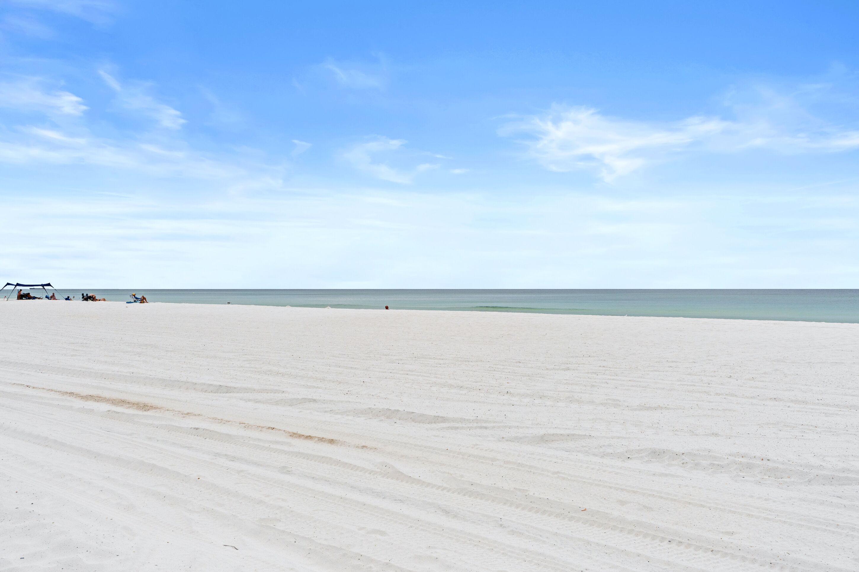 A wide, sandy beach with a clear sky and calm sea.
