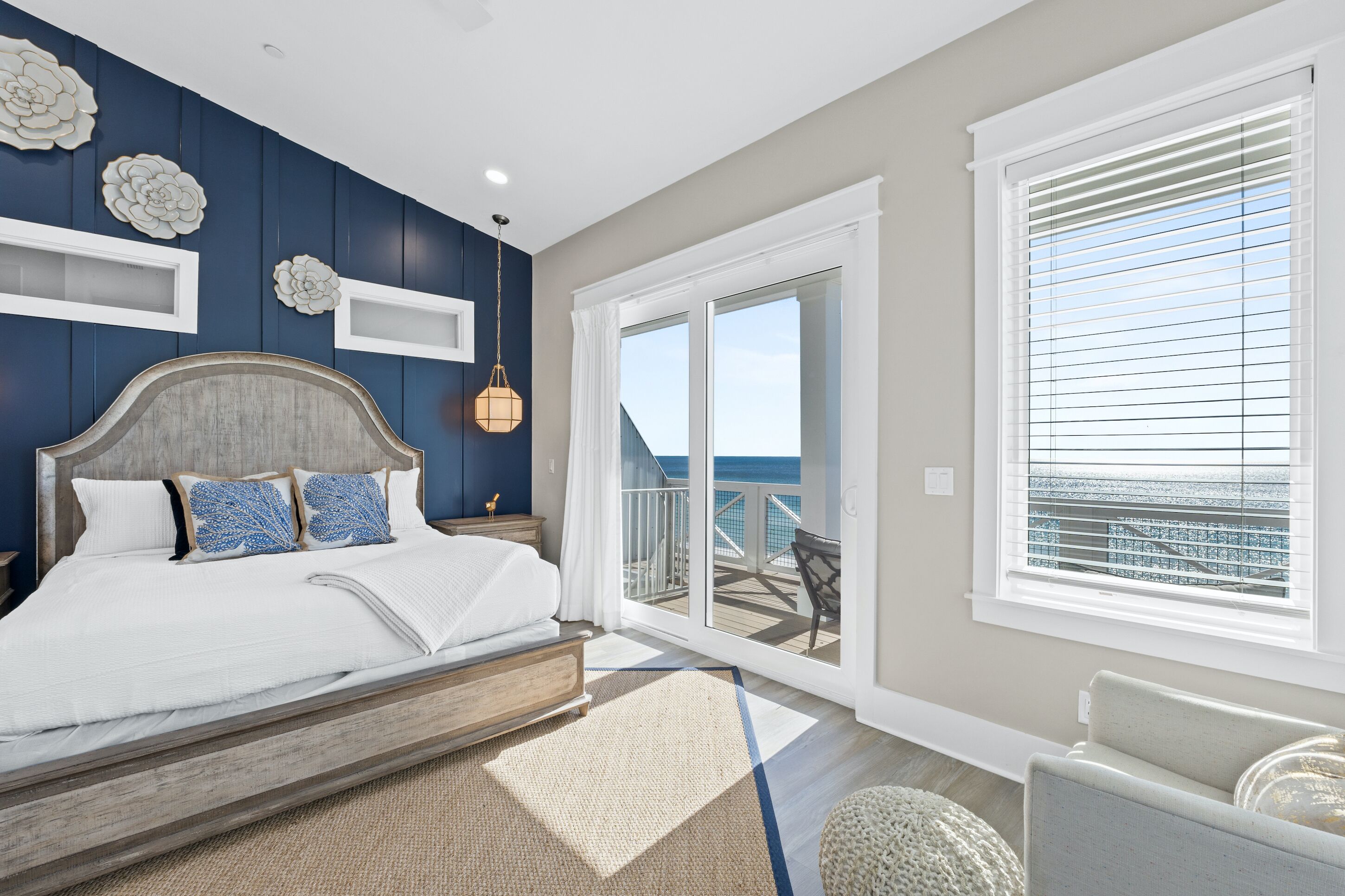 A bedroom with a large bed, a view of the ocean through a sliding glass door, and a balcony with a view of the ocean.