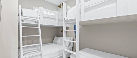 Une chambre avec un lit superposé, une échelle, une petite table et une étagère fixée au mur.