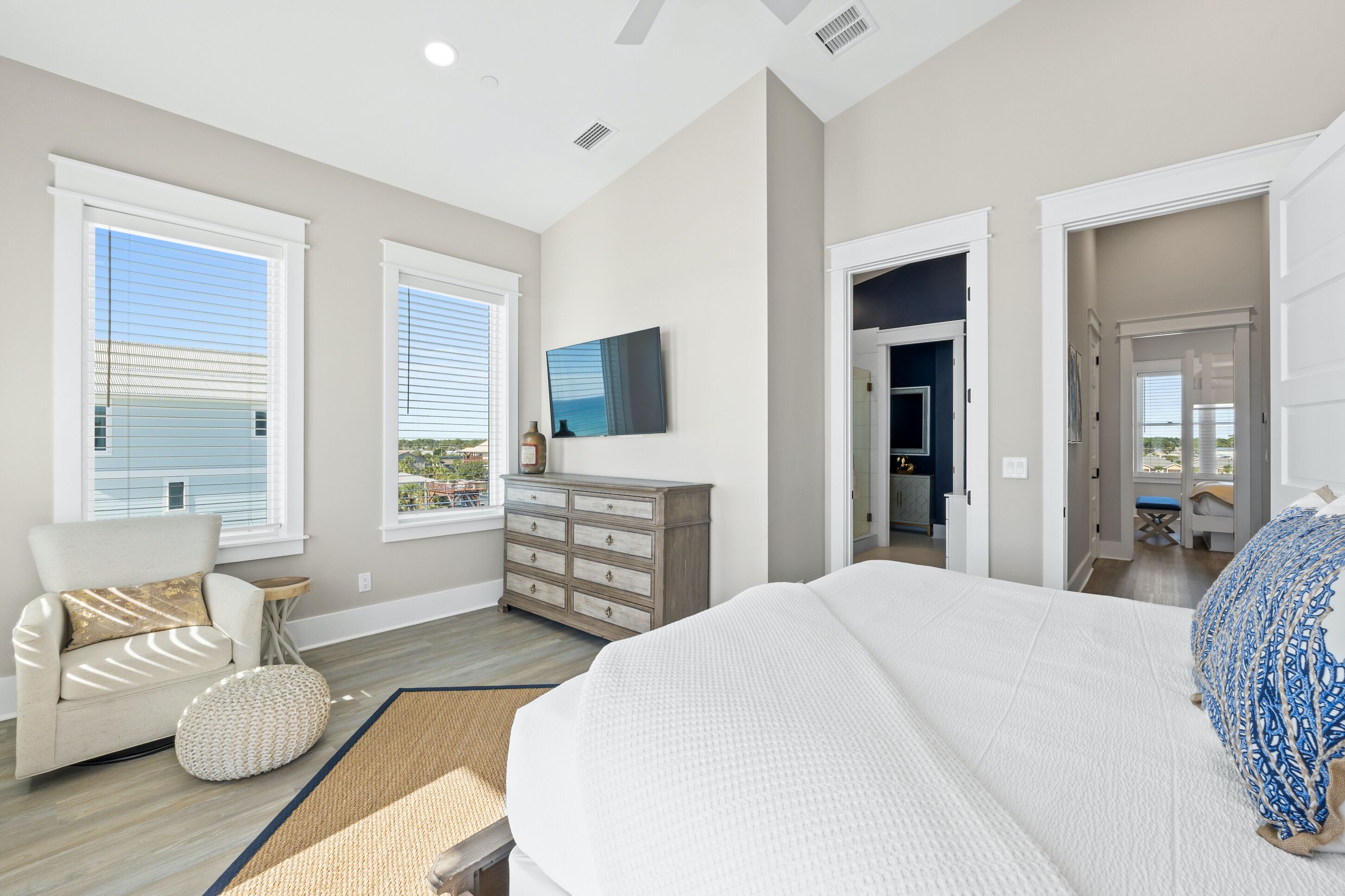A bedroom with a large bed, a dresser, a chair, and a view of the outside.