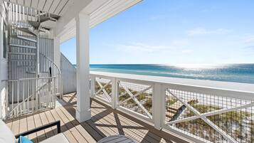 Una terraza de madera con barandilla blanca, una escalera y vista a la playa.