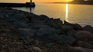 Eine felsige Küstenlinie mit einem Leuchtturm bei Sonnenuntergang.