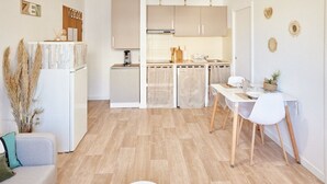 Eine moderne Küche mit hellen Holzschränken, einem Essbereich mit weißen Stühlen und einer kleinen Sitzecke mit einer Couch.