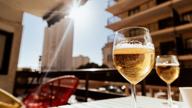 A glass of white wine on a balcony with a view of a building and a red chair. - Apt. Urbanization Las Lanzas, Muchavista beach (Fabraquer)