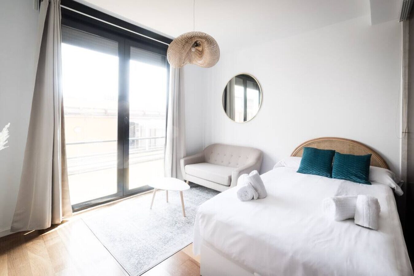 Ein modernes Hotelzimmer mit einem großen Bett, einem runden Spiegel, einer Couch und einer Pendelleuchte.