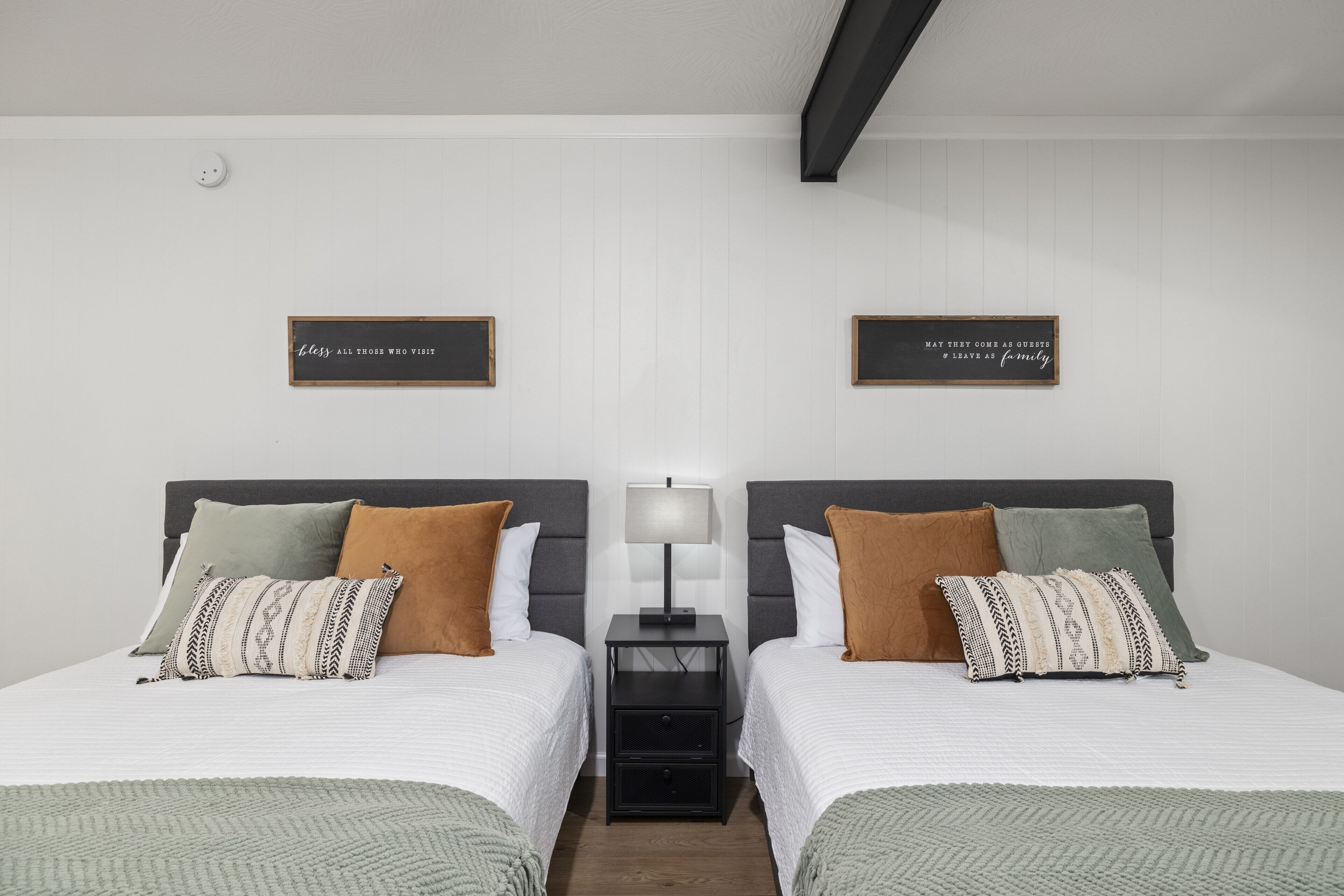 A twin room with two beds, a nightstand with a lamp, and two wall-mounted signs.