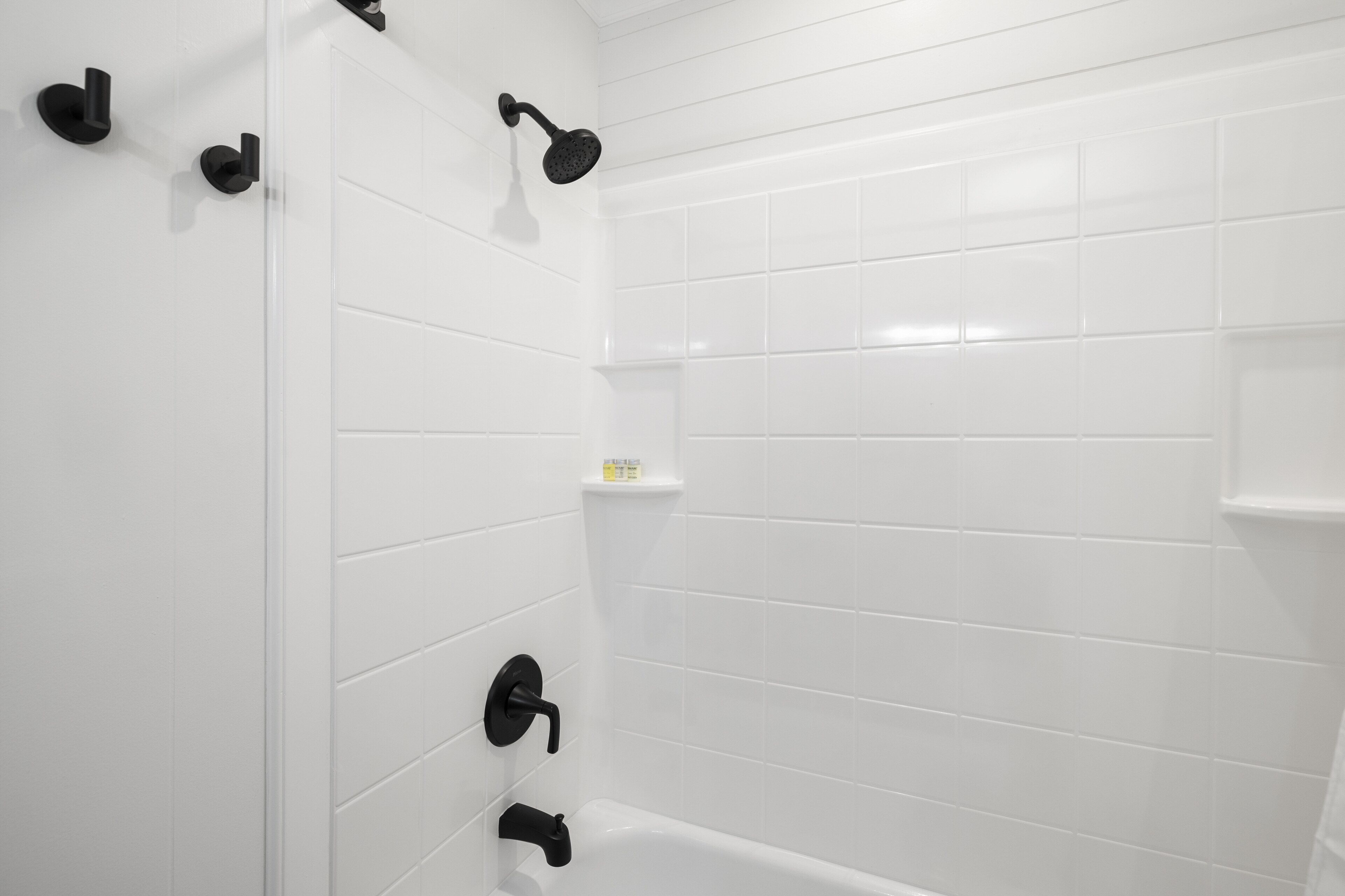 A bathroom with white tiled walls, a white bathtub, and black fixtures.