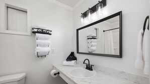 A modern bathroom with a white toilet, a sink with a black faucet, a towel rack with white towels, a mirror with a black frame, and a towel rack with a 'hotels' sign. - The Lofts on Indian Point (Branson)