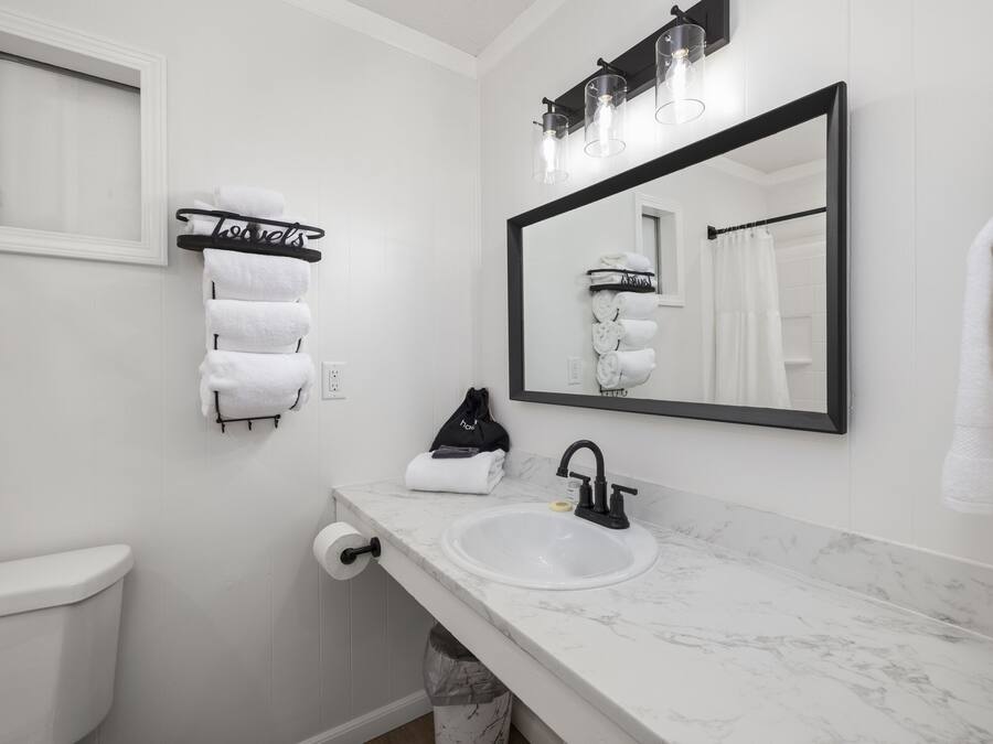 Un baño moderno con inodoro blanco, lavamanos con grifo negro, toallero con toallas blancas, espejo con marco negro y toallero con un letrero que dice 'hoteles'.