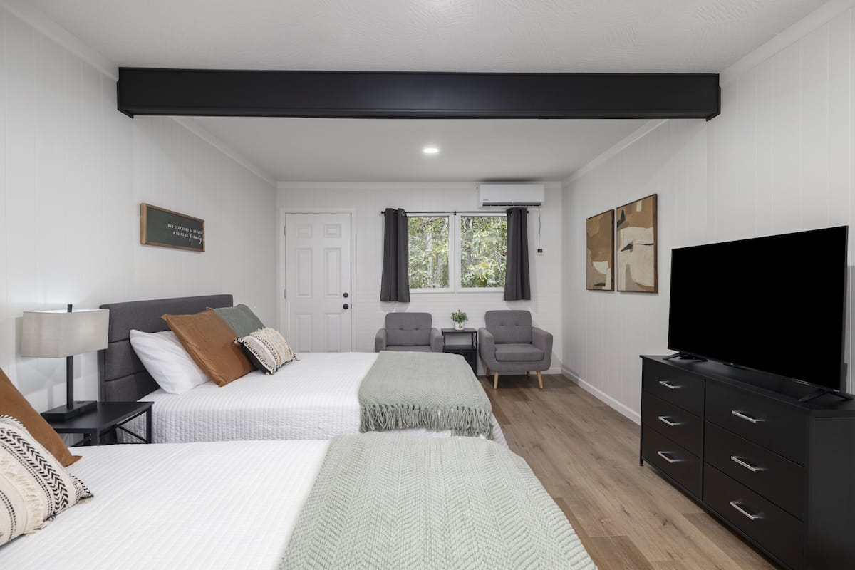 A hotel room with two beds, a TV, a desk, and a chair.
