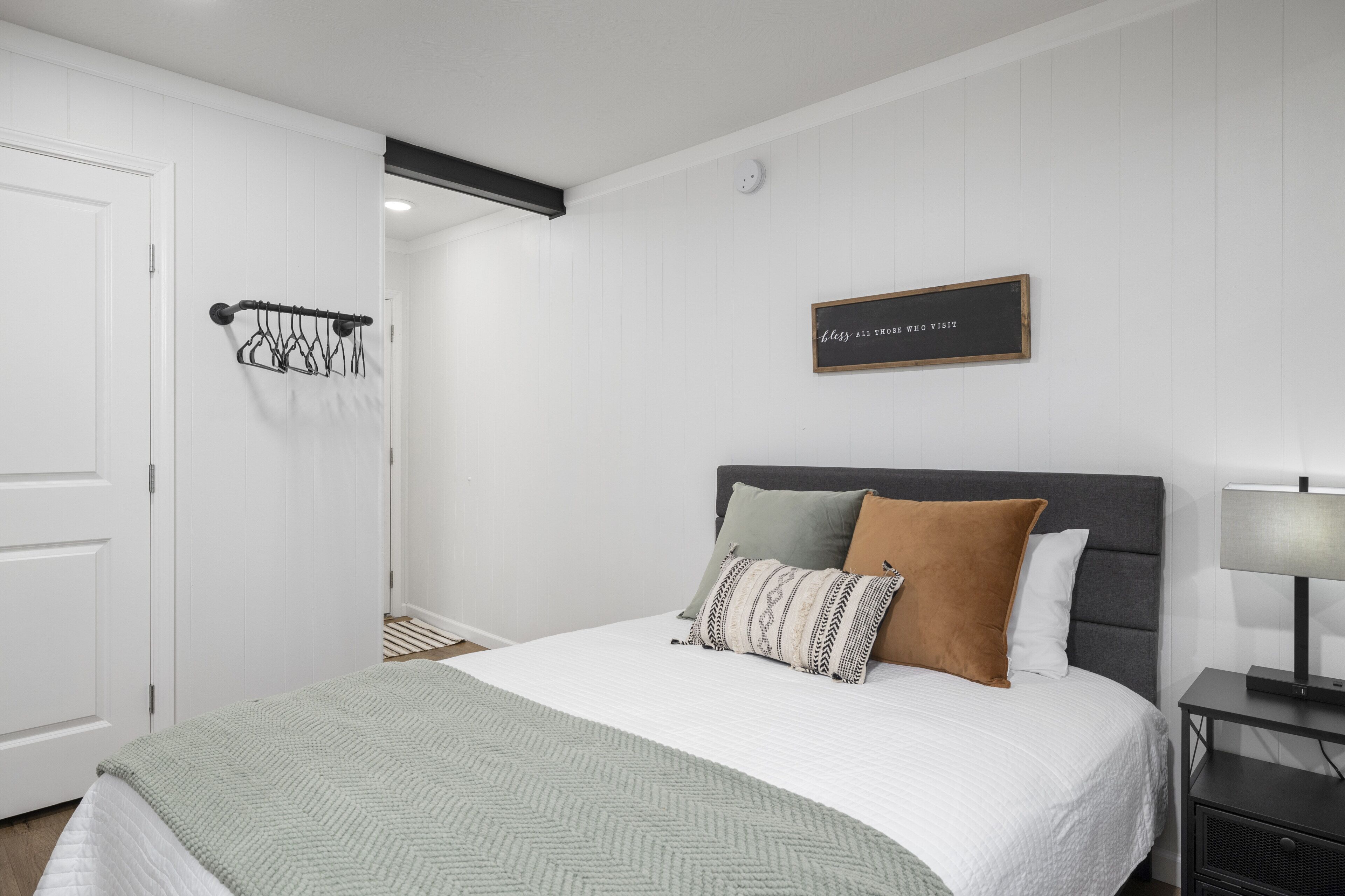 Un dormitorio ordenado con cama, mesita de noche y un cartel en la pared.
