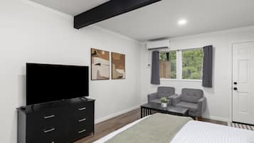 A modern bedroom with a bed, a TV, a desk, two chairs, and artwork on the wall.