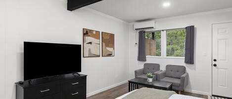 Une chambre à coucher moderne, avec un lit, une télévision, un bureau, deux chaises et des œuvres d’art accrochées au mur.