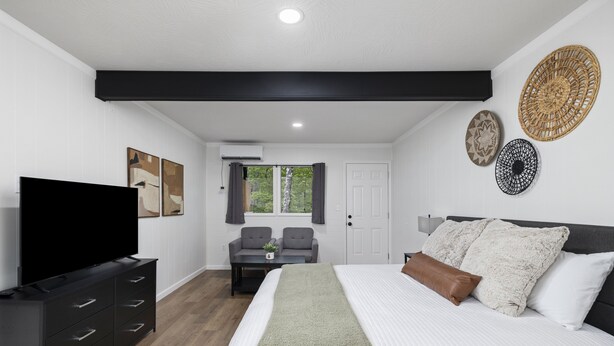 A modern bedroom with a large bed, a flat-screen TV, a sofa, and two decorative wall hangings. - The Lofts on Indian Point (Branson)