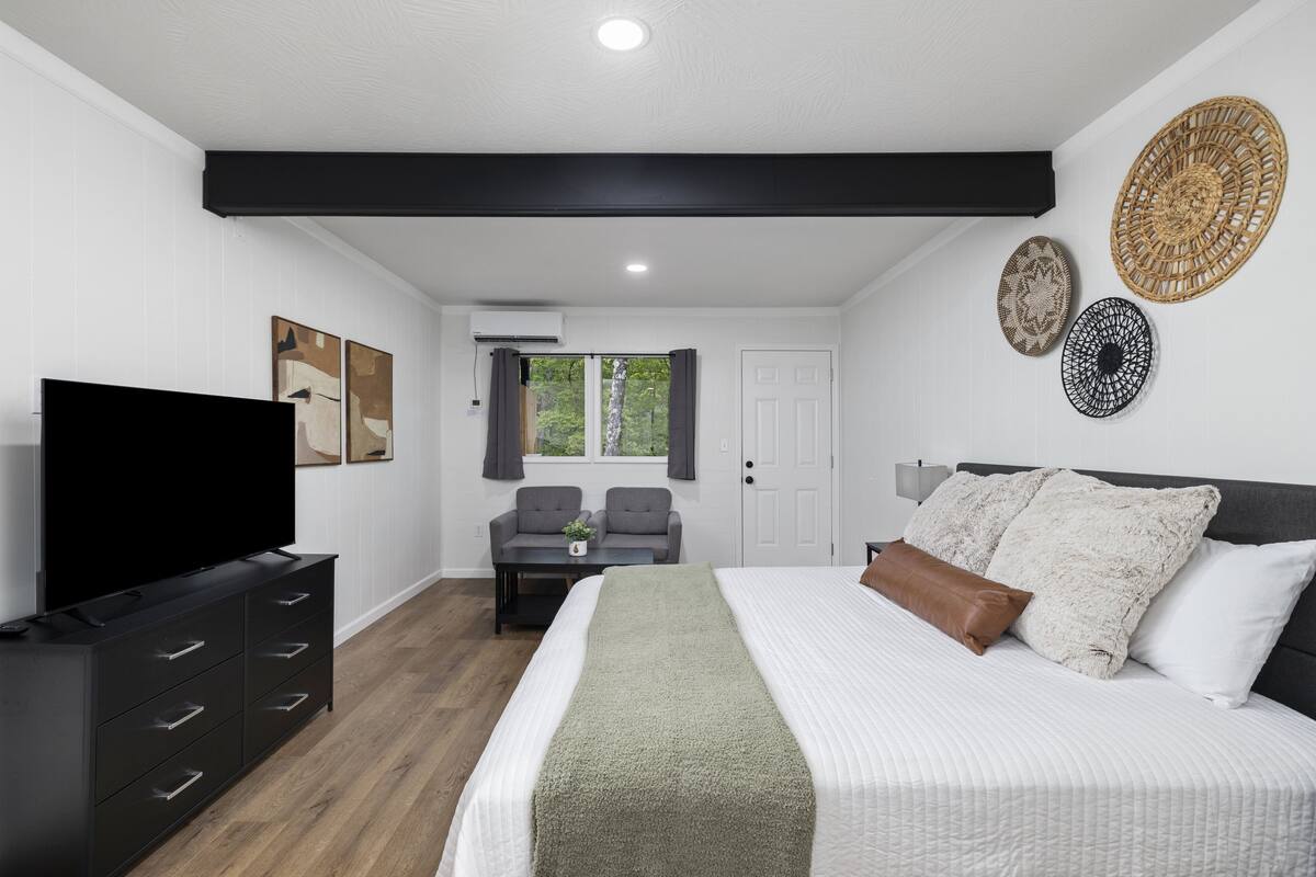 A modern bedroom with a large bed, a flat-screen TV, a sofa, and two decorative wall hangings.
