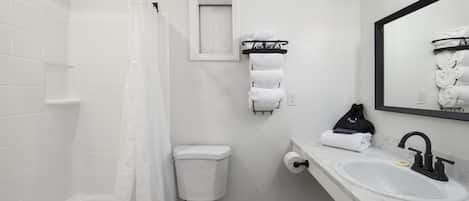 A bathroom with a white bathtub, toilet, and sink. There is a towel rack with towels and a black bag hanging on it.