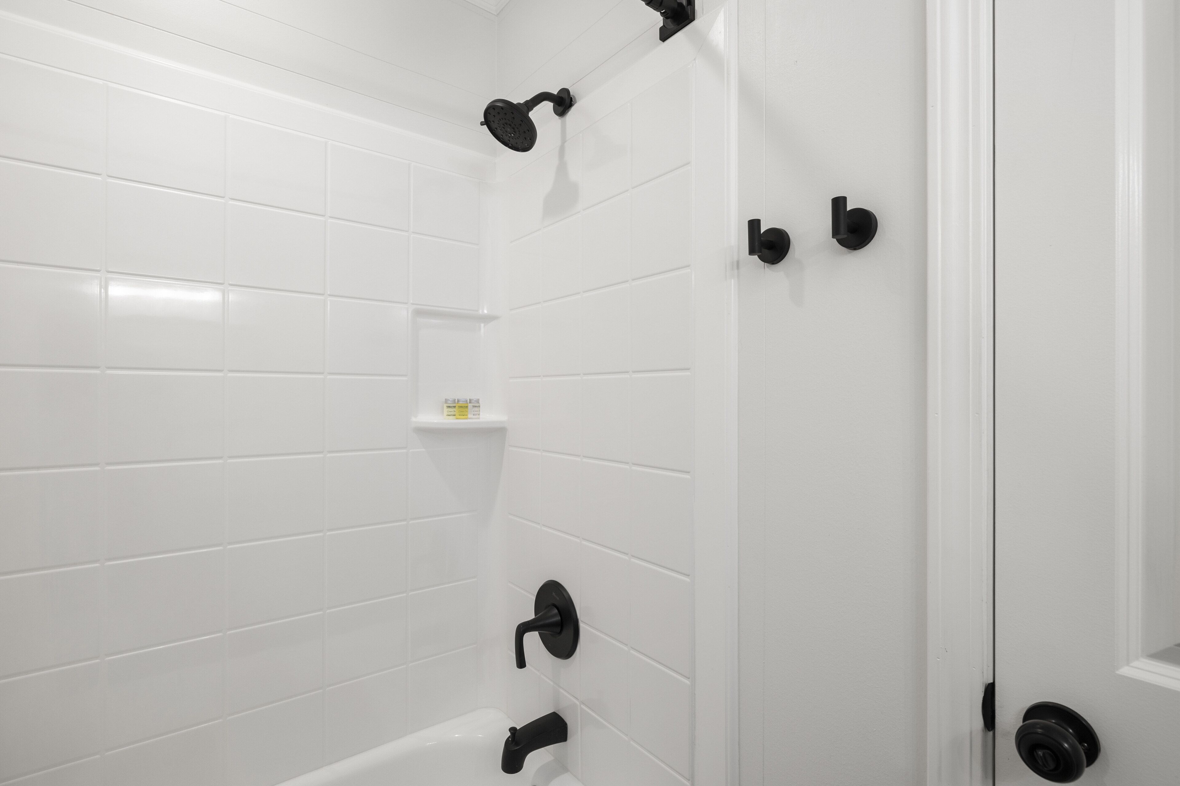 A bathroom with white tiled walls, a white bathtub, and black fixtures.