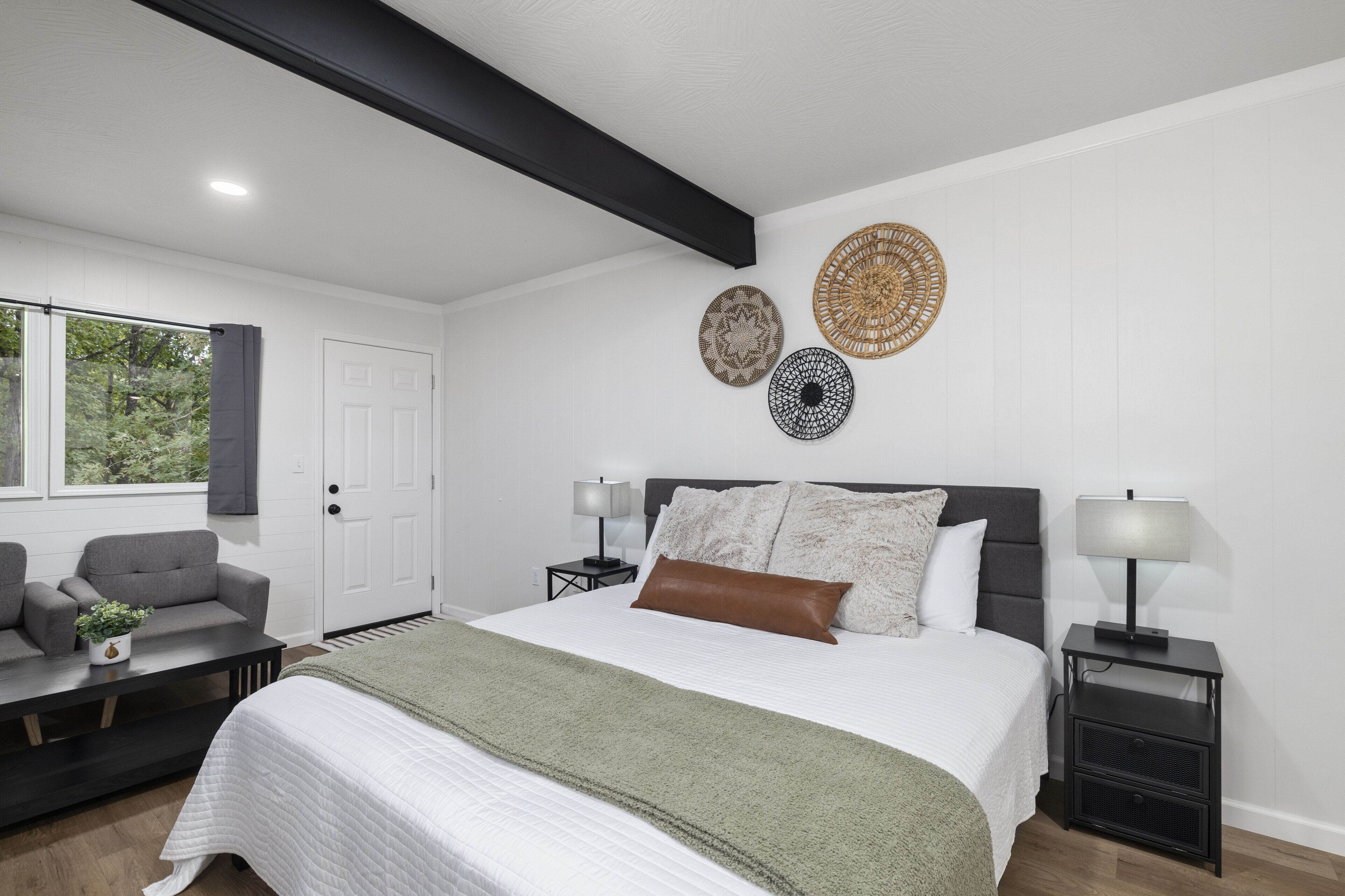 A modern bedroom with a large bed, bedside tables, a sofa, and decorative wall hangings.