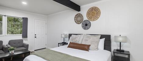 A modern bedroom with a large bed, bedside tables, a sofa, and decorative wall hangings.