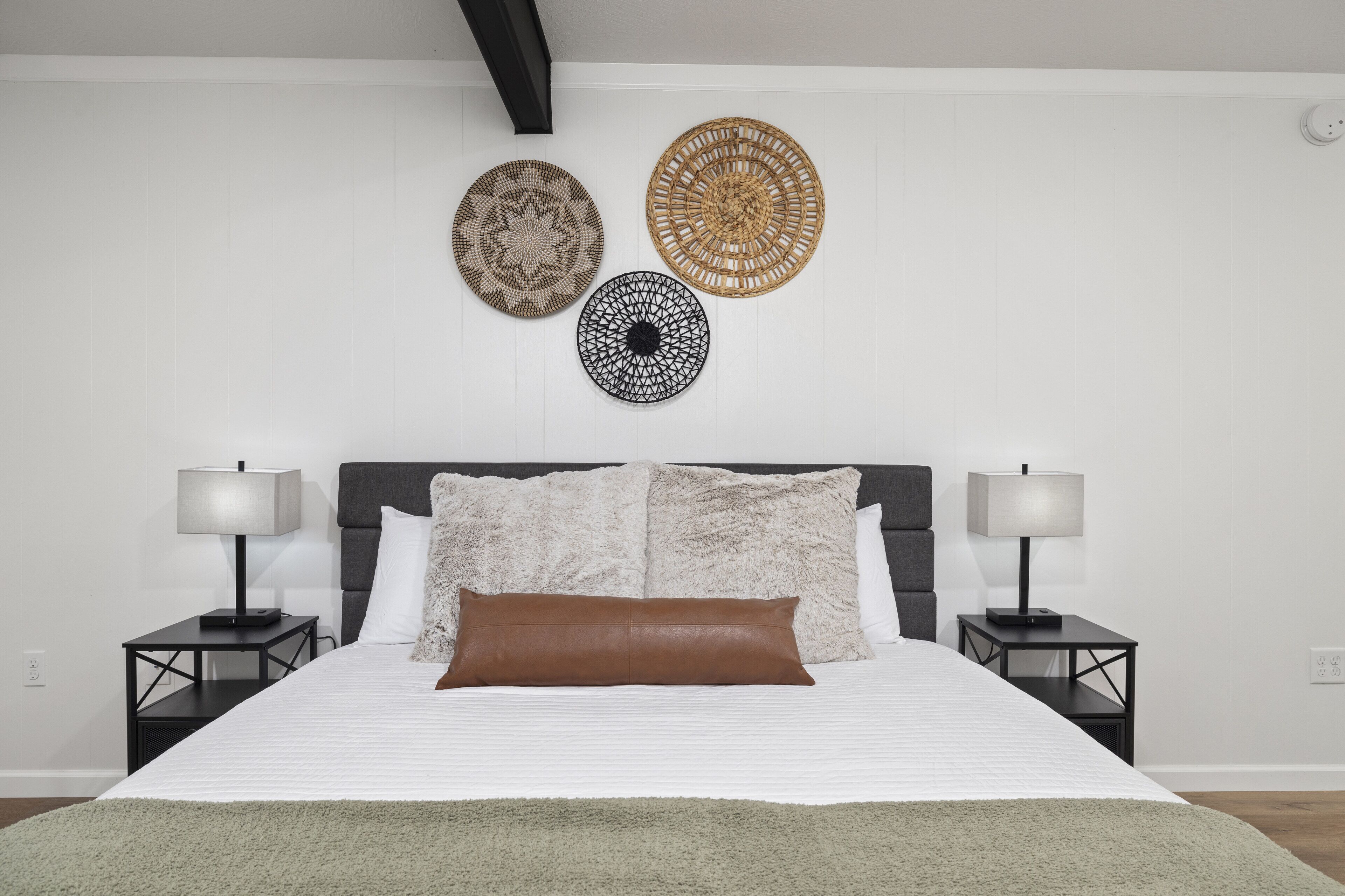 A neatly arranged bedroom with a large bed, two bedside tables with lamps, and three wall-mounted decorative items.