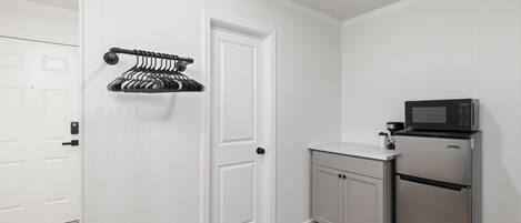 A compact kitchen with white cabinetry, a stainless steel refrigerator, and a microwave.