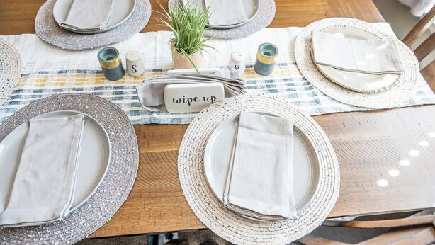 A dining table set with white plates, napkins, and a small potted plant. - Stoney Oasis (Charleston)