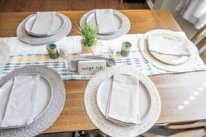 Une table à manger dressée avec de l’assiette blanche, des serviettes et une petite plante en pot.