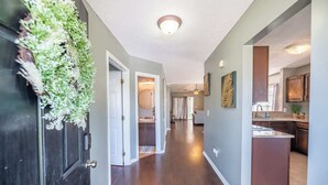 A hallway with a dark wooden door, a plant, and a kitchen area with a countertop and cabinets. - Stoney Oasis (Charleston)