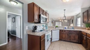 A modern kitchen with dark wood cabinets, a stainless steel microwave, and a white dishwasher. - Stoney Oasis (Charleston)