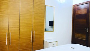 A bedroom with a bed, a wardrobe, a bedside table, and a mirror. - Charming 1-bed Apartment in Victoria Island, Lagos (Lagos)