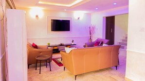 A modern living room with a sofa, a small table, and a TV mounted on the wall. - Captivating 3-bed Apartment in Lagos (Lekki)