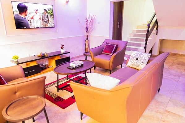 A modern living room with a sofa, armchairs, a coffee table, and a TV mounted on the wall. - Captivating 3-bed Apartment in Lagos (Lekki)