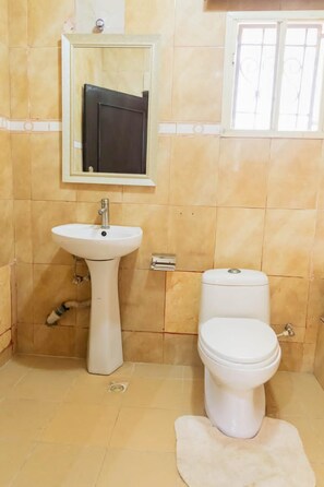 A bathroom with a pedestal sink, a toilet, and a mirror above the sink. - Captivating 3-bed Apartment in Lagos (Lekki)